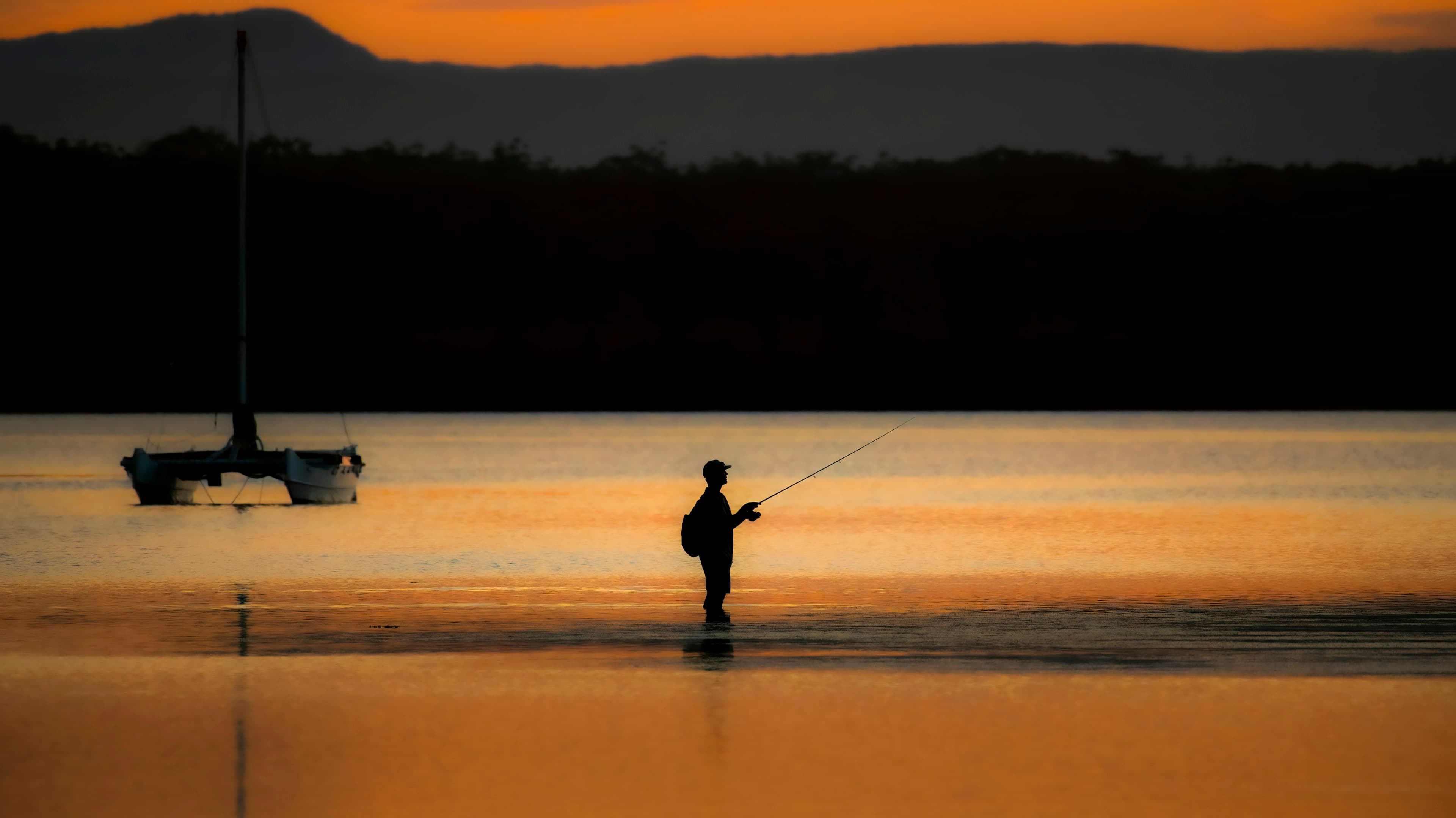 Angler standing in calm lake water at golden hour, casting a fishing line