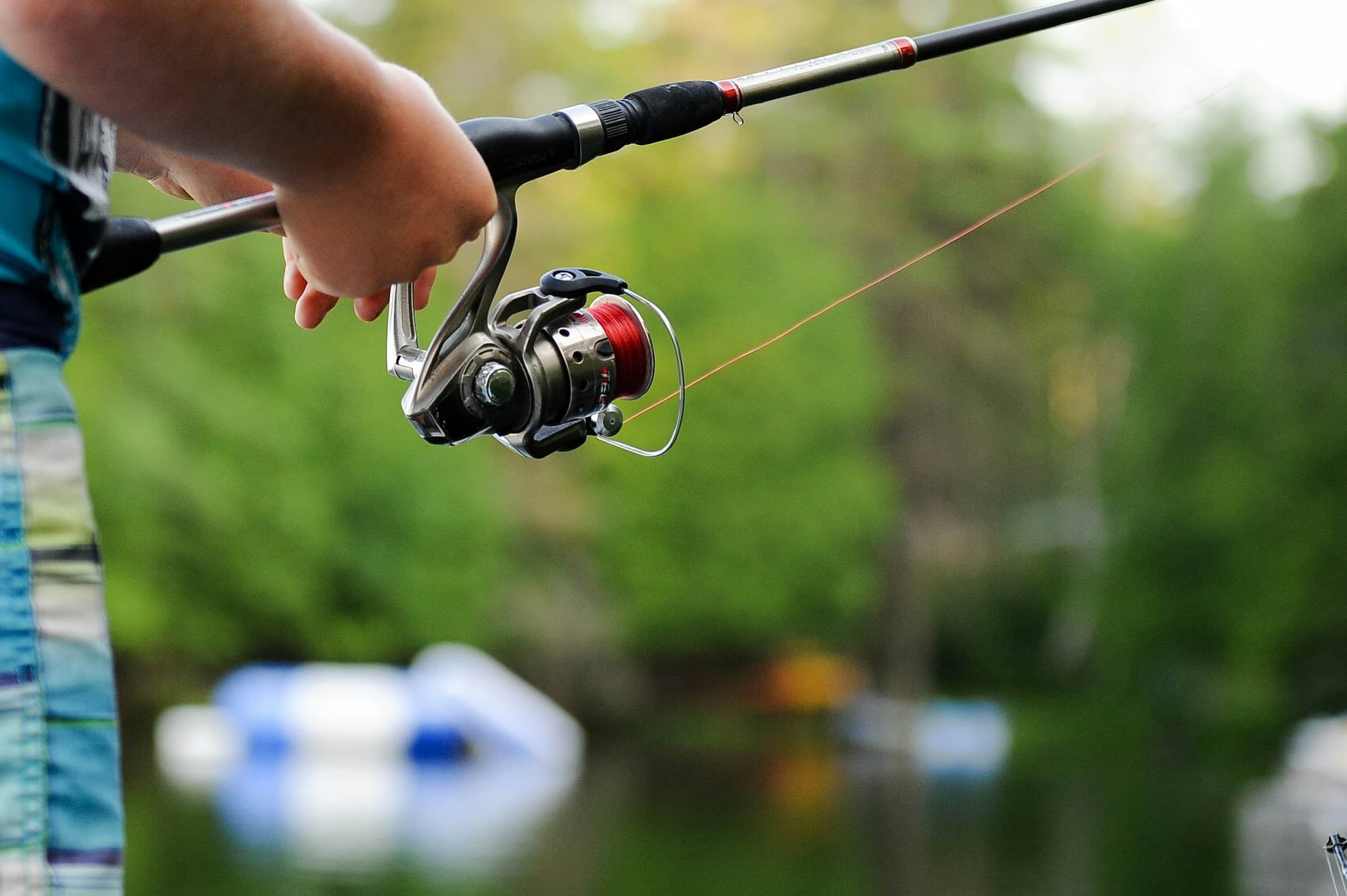 Close-up of an angler's hand on a spinning reel by the water